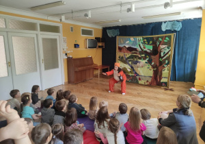 Dzieci siedzą na materacach i oglądają teatrzyk o przyjaźni, na scenie znajduje się Pani przebrana za liska wykonuje przysiady.