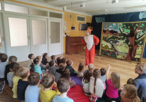 Dzieci siedzą na materacach i oglądają teatrzyk o przyjaźni, na scenie znajdują się Pani przebrana za liska nad czymś się zastanawia.