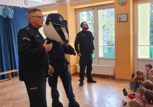 Panowie policjanci przedstawiają dzieciom policyjną maskotkę borsuka i rozmawiają o bezpieczeństwie.