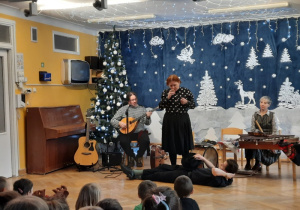 Pani imituje dźwięk ptaka i budzi śpiącego na środku muzyka.