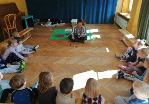 Pani Ania siedzi na podłodze i pokazuje dzieciom ślimaka. Opowiada dzieciom siedzącym w półokręgu o nim.
