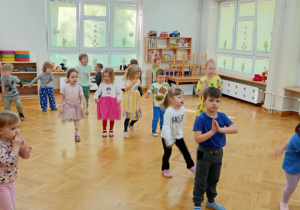Dzieci stoją w rozsypce na sali i powtarzają taneczne ruchy za prowadzącą zajęcia z zumby.