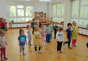 Dzieci stoją w rozsypce na sali i powtarzają taneczne ruchy za prowadzącą zajęcia z zumby.