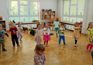 Dzieci stoją w rozsypce na sali i powtarzają taneczne ruchy za prowadzącą zajęcia z zumby.