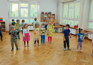 Dzieci stoją w rozsypce na sali i powtarzają taneczne ruchy za prowadzącą zajęcia z zumby.