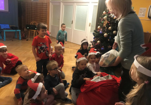 Pani Dyrektor razem z dziećmi wypakowują prezenty z worka od Świętego Mikołaja.