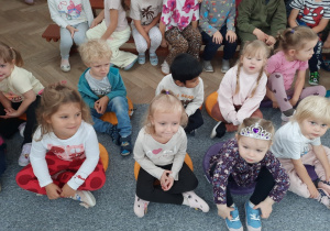 Dziewczynki i chłopcy z młodszej grupy siedzą na poduszkach i czekają na rozpoczęcie przedstawienia.