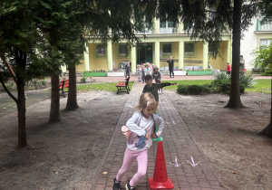 Dzieci wykonują bieg slalomem wokół pachołków.