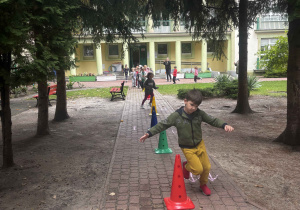 Dzieci wykonują bieg slalomem wokół pachołków.