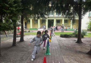 Dzieci wykonują bieg slalomem wokół pachołków.
