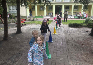 Dzieci wykonują bieg slalomem wokół pachołków.