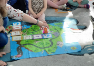 Dzieci siedzą na dywanie, a prowadząca warsztaty pokazuje dzieciom, jak należy prawidłowo ustawić robocika ślimaka.