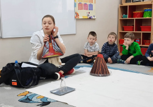 Prowadząca warsztaty prezentuje dzieciom model budowy wulkanu w przekroju.