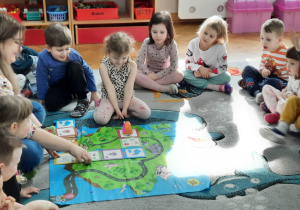 Dzieci siedzą na dywanie, a jedna dziewczynka prowadzi robocika ślimaka po trasie ze specjalnych puzzli.