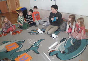 Dzieci siedzą na dywanie, a prowadząca warsztaty z robotyki tłumaczy im, jak mają korzystać z tabletów.