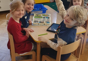 Dzieci siedzą przy stole i prezentują robota z klocków LEGO ułożonego na zajęciach z robotyki.