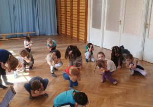 Dzieci powtarzają ruchy taneczne za trenerką zumby kucając i zasłaniając głowę rękami.