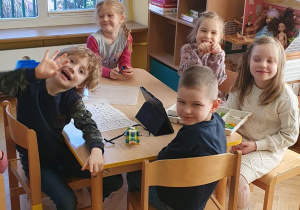 Dzieci siedzą przy stoliku i prezentują zbudowanego przez siebie robocika z klocków LEGO.