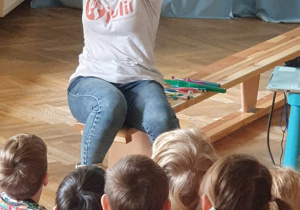 Dzieci siedzą na ławkach, a prowadząca warsztaty prezentuje im duży model ludzkiej jamy ustnej.