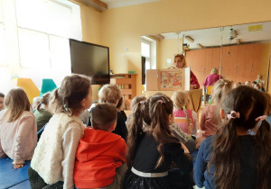 Dzieci siedzą na materacach i oglądają przygotowane przez nauczycielkę teatrzyk Kamishibai o emocjach na podstawie przygód Kubusia Puchatka.