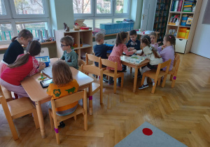 Dzieci siedzą przy stolikach i układają robota z klocków LEGO na podstawie instrukcji wyświetlanej na tablecie na warsztatach z robotyki.