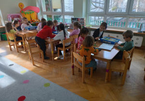 Dzieci siedzą przy stolikach i układają robota z klocków LEGO na podstawie instrukcji wyświetlanej na tablecie na warsztatach z robotyki.