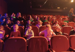 Dzieci siedzą na widowni w teatrze czekając na rozpoczęcie spektaklu.