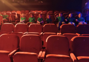 Dzieci siedzą na widowni w teatrze czekając na rozpoczęcie spektaklu.