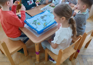 Dzieci siedzą przy stoliku i za pomocą instrukcji wyświetlanej na tablecie budują roboty z klocków LEGo na warsztatach z robotyki i programowania.