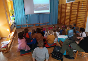 Dzieci siedzą na materacach i oglądają prezentację nt. mostów na warsztatach z Fundacji "Szkatułka".