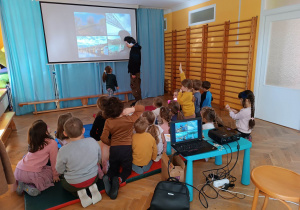 Dzieci siedzą na materacach i oglądają prezentację nt. mostów na warsztatach z Fundacji "Szkatułka".