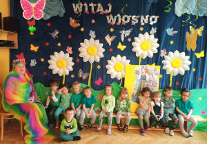 Dzieci ubrane na zielono pozują do grupowego zdjęcia z Panią Wiosną oraz jej podobizną.