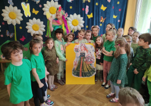 Dzieci ustawione w półkolu wspólnie z jedną z Pań przebraną za Panią Wiosną prezentują ułożone puzzle z podobizną Wiosny.