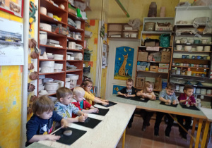 Dzieci siedzą przy stolikach i lepią z gliny na warsztatach ceramicznych w pracowni ceramicznej Amfora.
