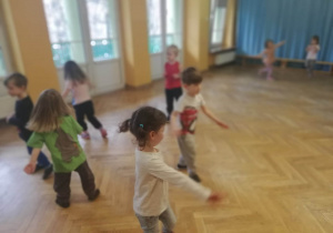 Dzieci ustawione w rozsypce na sali gimnastycznej poruszają się swobodnie do dowolnej muzyki.