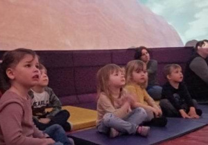 Dzieci siedzą na materacach i odbywają wycieczkę w kosmos za pomocą specjalnego pokazu w mobilnym planetarium w wielkim balonowym namiocie.