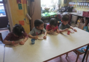 Dzieci siedzą przy stoliku i malują specjalnymi farbami wcześniej ulepione własnoręcznie talerzyki ceramiczne.
