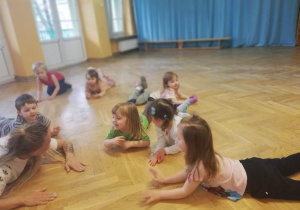 Dzieci wspólnie z trenerką leżą na podłodze odpoczywając po zakończeniu zajęć z zumby.