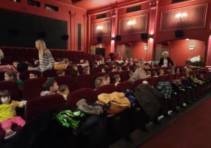 Dzieci siedzą na fotelach w kinie i czekają na rozpoczęcie seansu filmowego.