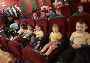Dzieci siedzą na fotelach w kinie i czekają na rozpoczęcie seansu filmowego.