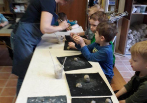 Chłopcy siedzą przy stoliku i z pomocą prowadzącej warsztaty lepią z gliny na warsztatach ceramicznych w pracowni ceramicznej Amfora.