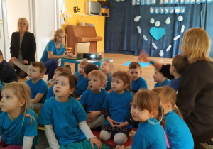 Dzieci ubrane na niebiesko oglądają prezentację multimedialną nt. świadomości o autyzmie.