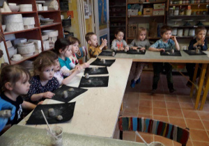 Dzieci siedzą przy stolikach i lepią z gliny na warsztatach ceramicznych w pracowni ceramicznej Amfora.