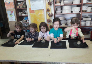 Dziewczynki siedzą przy stolikach i lepią z gliny na warsztatach ceramicznych w pracowni ceramicznej Amfora.