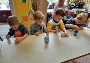 Chłopcy siedzą przy stoliku i malują specjalnymi farbami wcześniej ulepione własnoręcznie sówki ceramiczne.