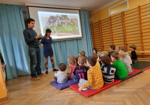 Dzieci siedzą na materacach i oglądają prezentację multimedialną nt. parków i przestrzeni zielonej w mieście.