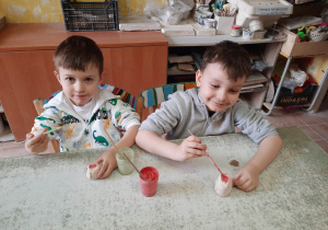 Chłopcy siedzą przy stoliku i malują specjalnymi farbami wcześniej ulepione własnoręcznie sówki ceramiczne.