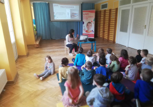 Dzieci siedzą na materacach i słuchają, jak prowadząca warsztaty stomatologiczne opowiada im z jakich zębów składa się jama ustna.