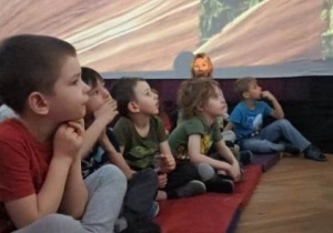 Dzieci siedzą na materacach i odbywają wycieczkę w kosmos za pomocą specjalnego pokazu w mobilnym planetarium w wielkim balonowym namiocie.