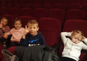Dziewczynki i chłopiec siedzą na fotelach w kinie i czekają na początek filmu.